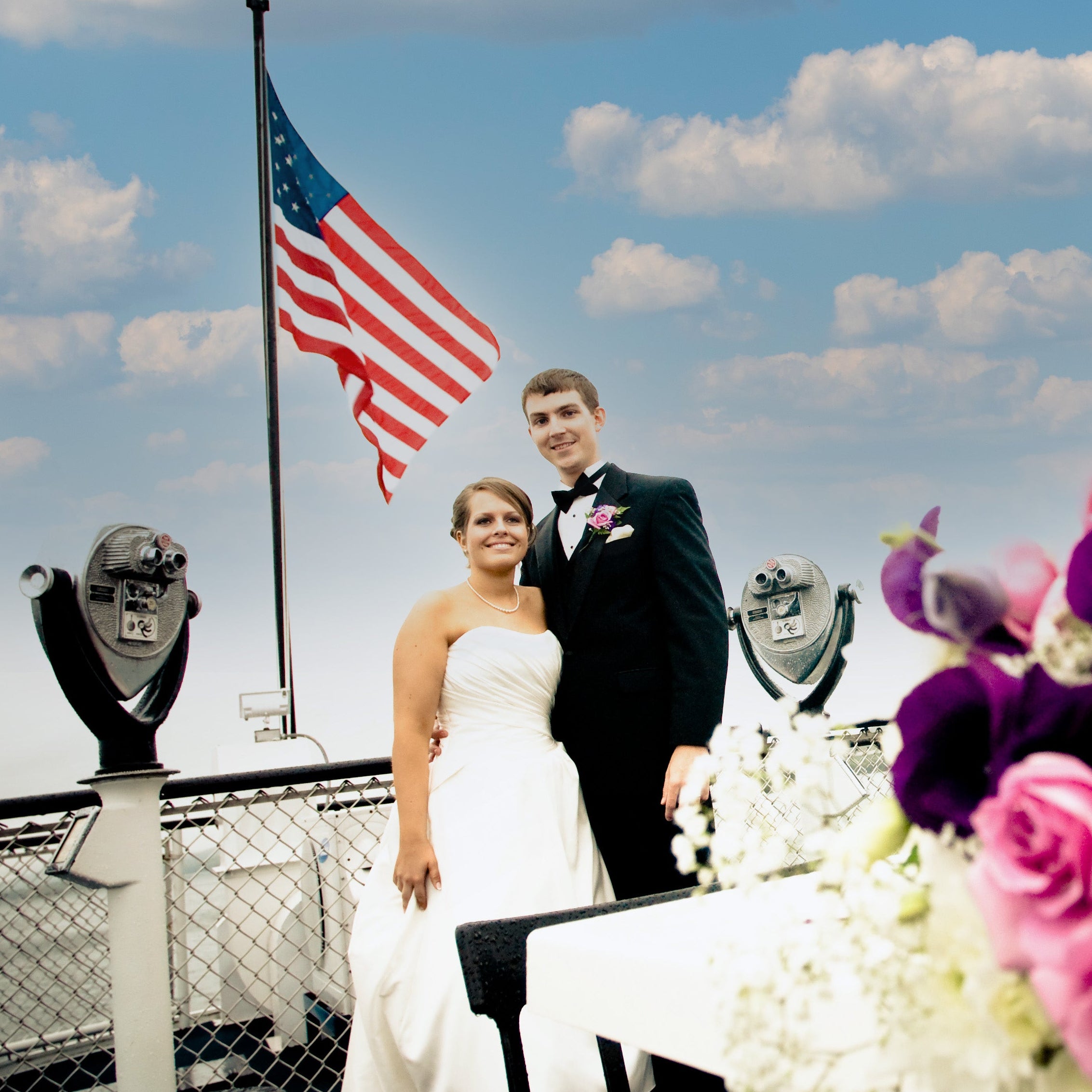 Wedding couple on a boat with an American flag and a floral arrangement in the foreground.